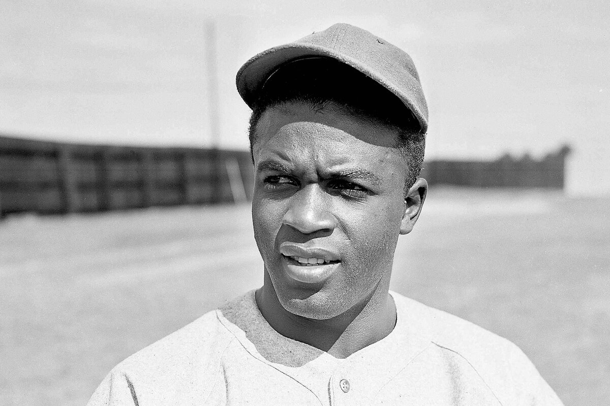 Jackie Robinson faces the camera wearing a baseball cap and uniform. 