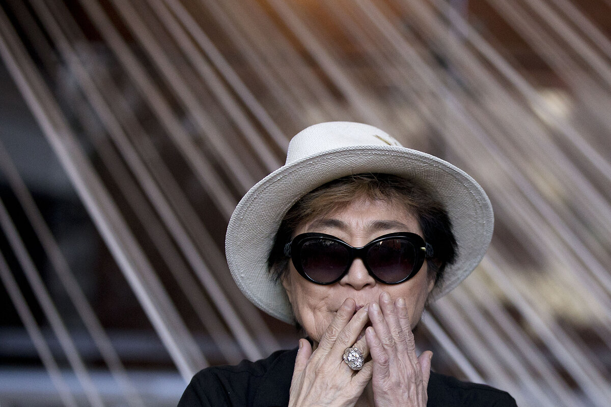 Yoko Ono in sunglasses and hat blows kisses. 