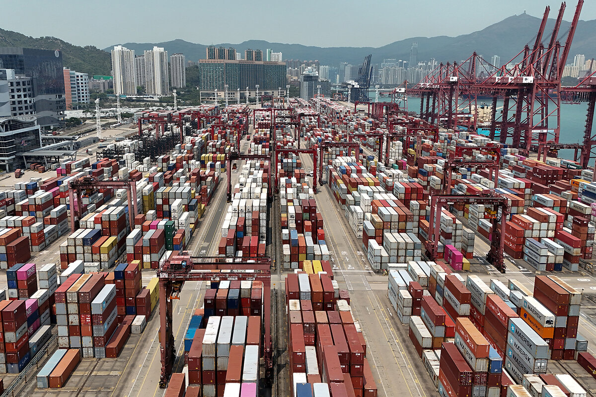 An overhead view shows hundreds of colorful, rectangular shipping containers that line port terminals in Hong Kong.