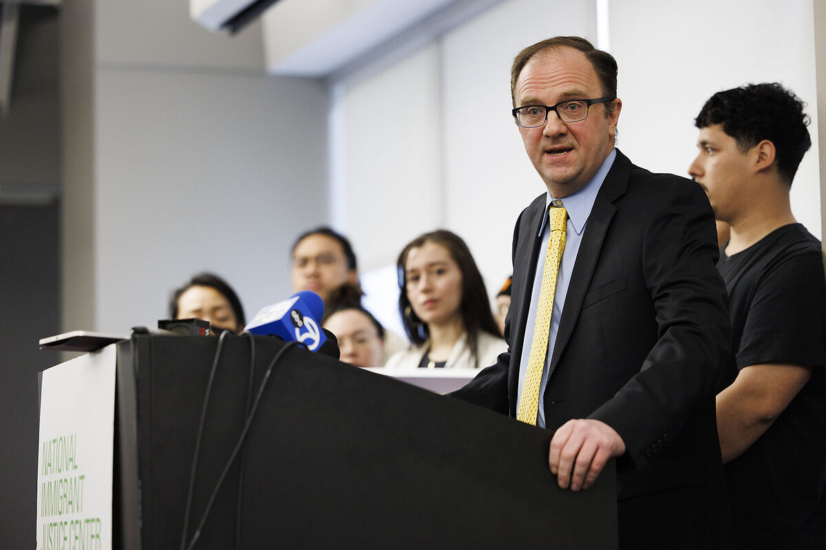 Mark Fleming speaks at an indoor podium, with some other people standing behind him.