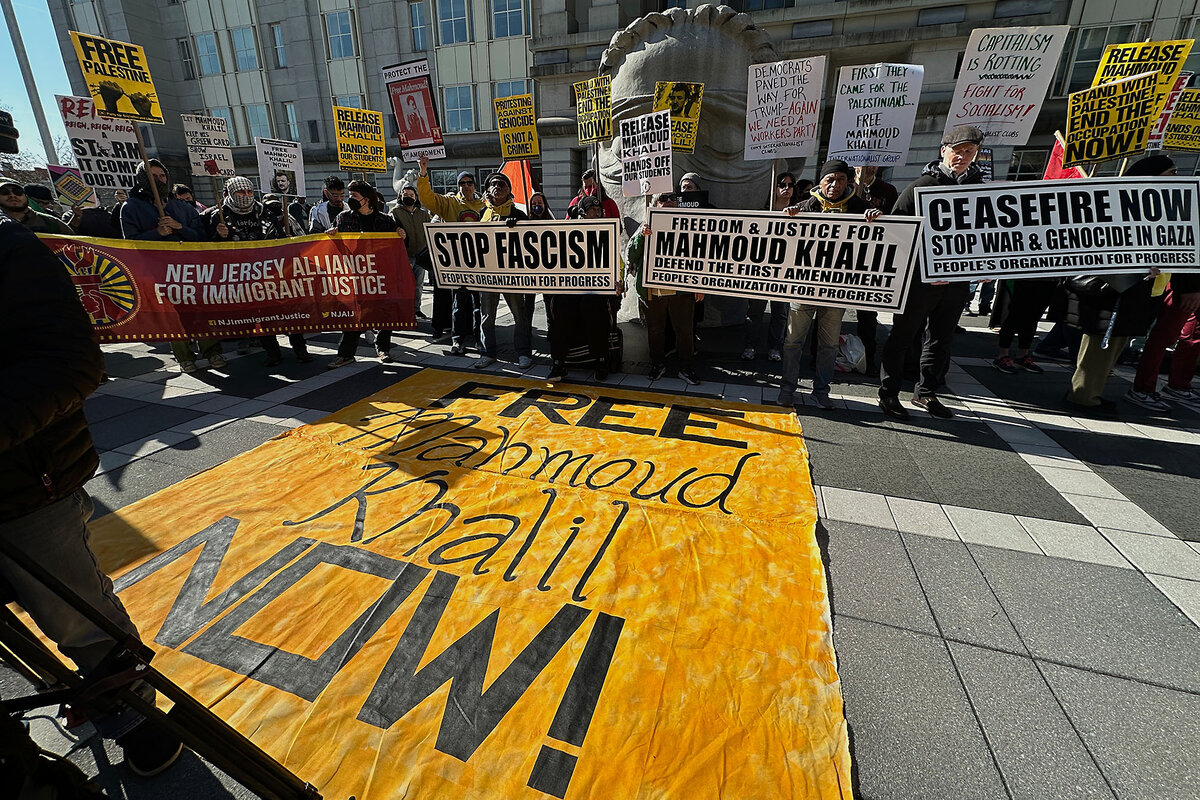 Protesters hold placards near a banner on the pavement that says, 'Free Mahmoud Khalil now!'