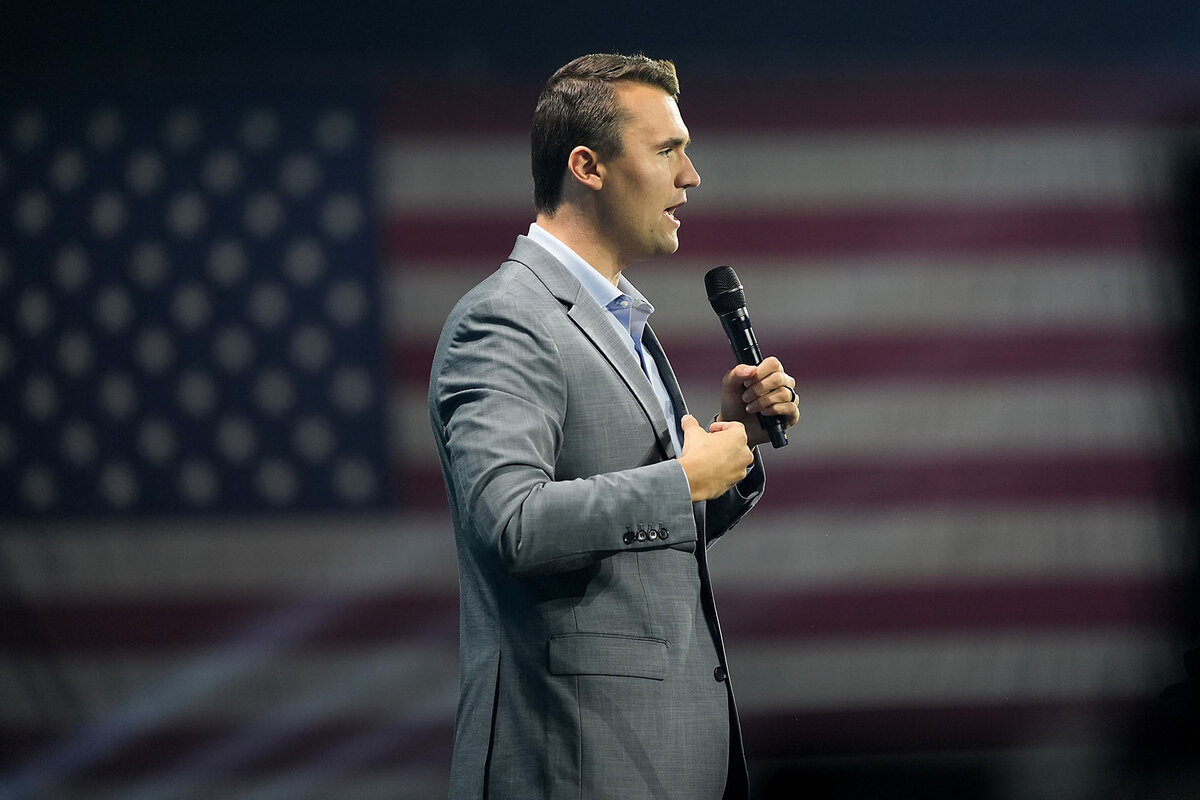 Turning Point USA founder Charlie Kirk stands before an American flag while speaking at a summit. 