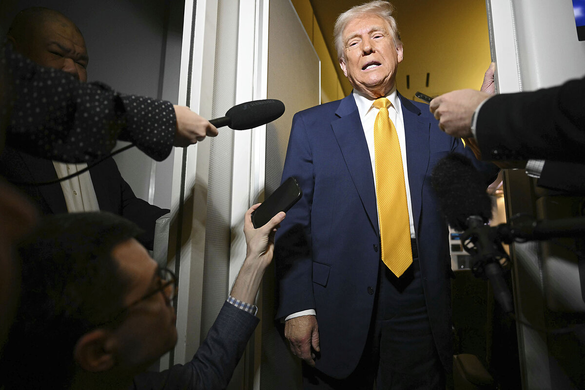 President Trump, in yellow necktie and navy blazer, looks down as he speaks into several reporters' microphones