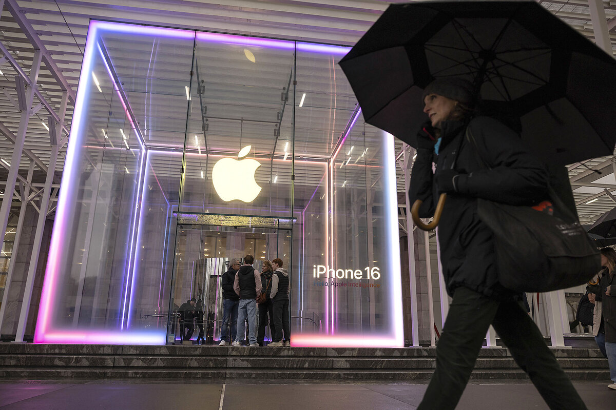 A person carrying a dark umbrella walks past the neon-lit Apple Store on Fifth Avenue in New York.