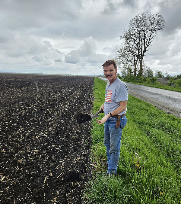Man in gray T-shirt and jeans stands next to a newly plowed field.