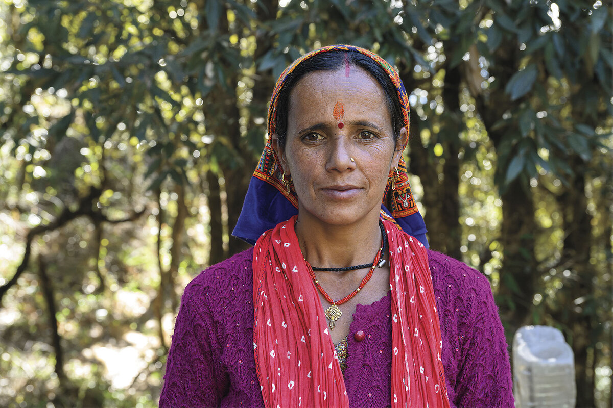 A woman wearing traditional head scarf and a bindi poses in front of trees.