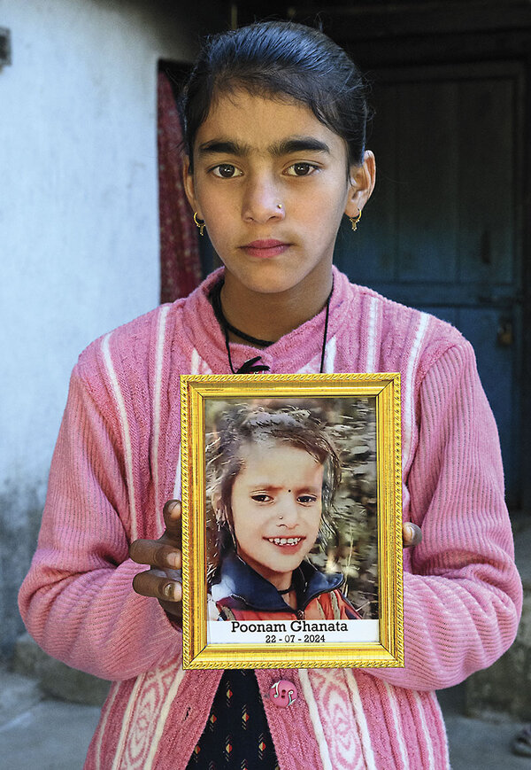 A girl in a pink sweater holds a framed portrait of another young girl.
