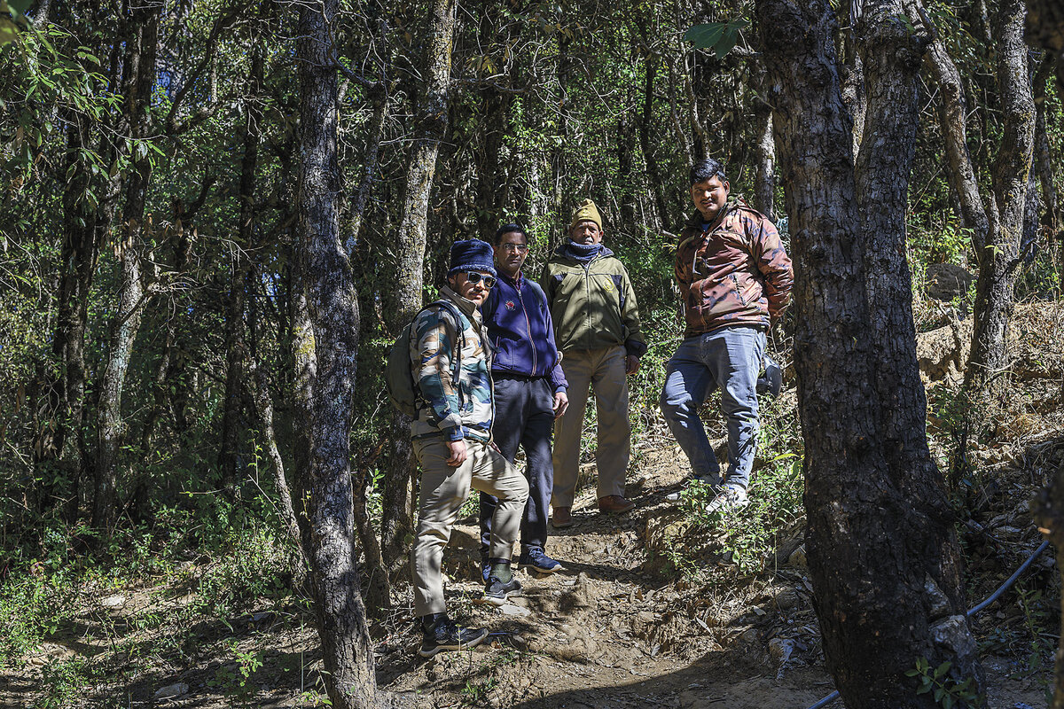 Four men, bundled up for cooler weather, stand in a sloped forest.