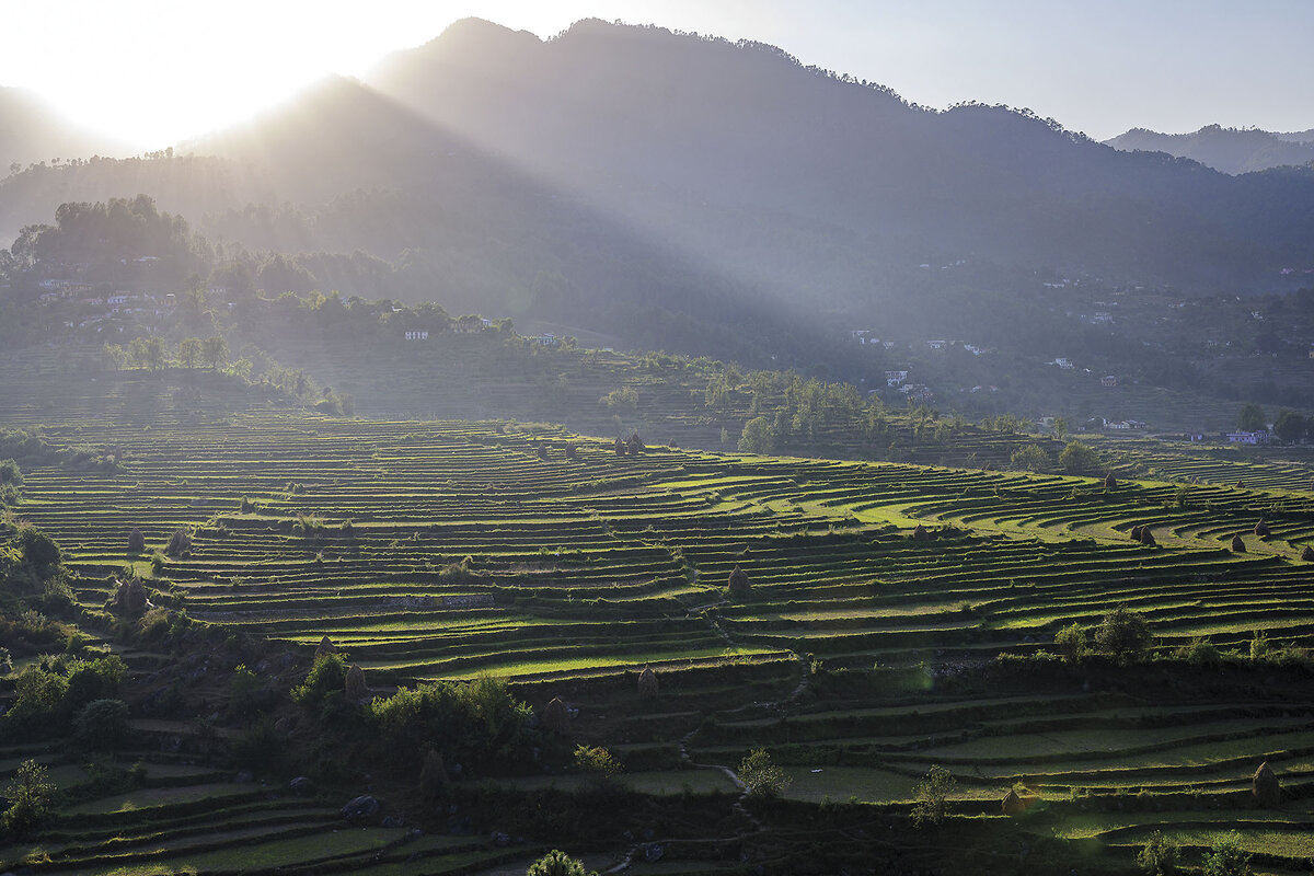 The sun shines over hazy mountains and rolling hills.