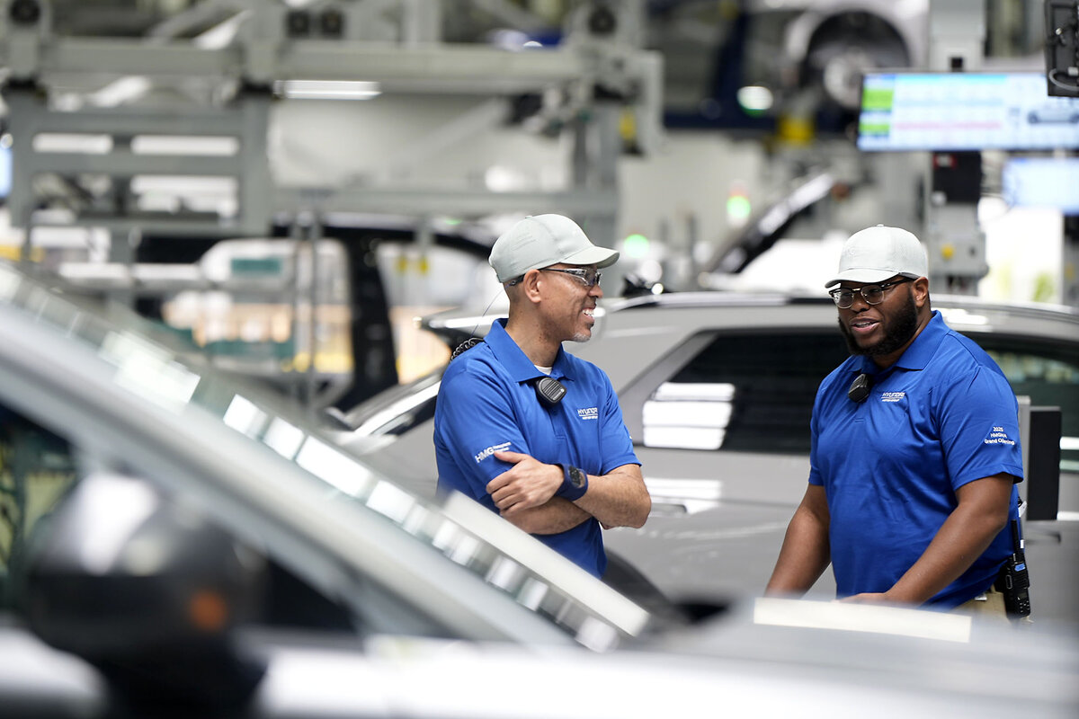 Two workers in blue shirts stand and talk amid a factory full of conveyor belts.