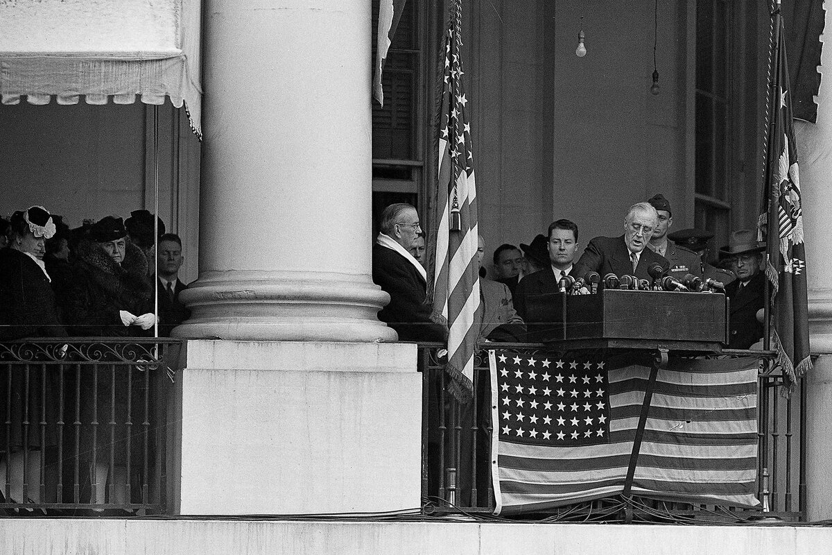 Franklin D. Roosevelt speaks from behind a podium, with an American flag displayed in front of it.