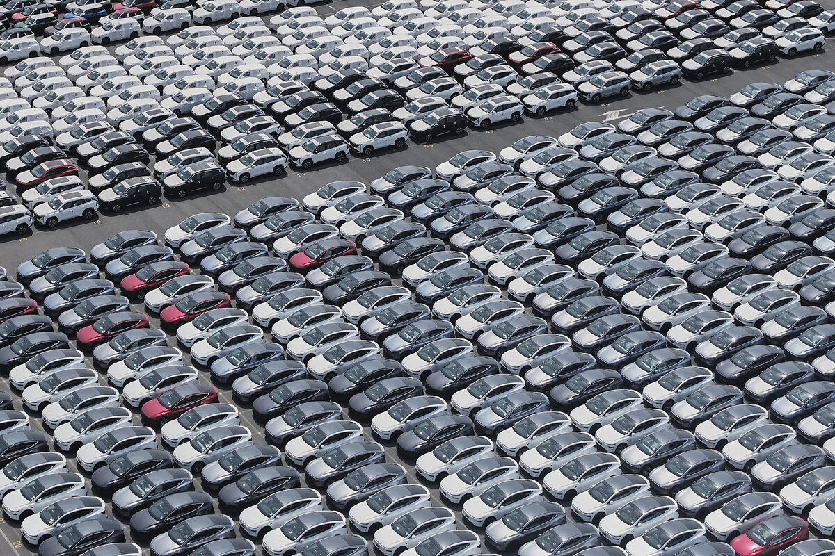 An aerial view shows dozens of cars parked tightly in rows in a port parking lot.