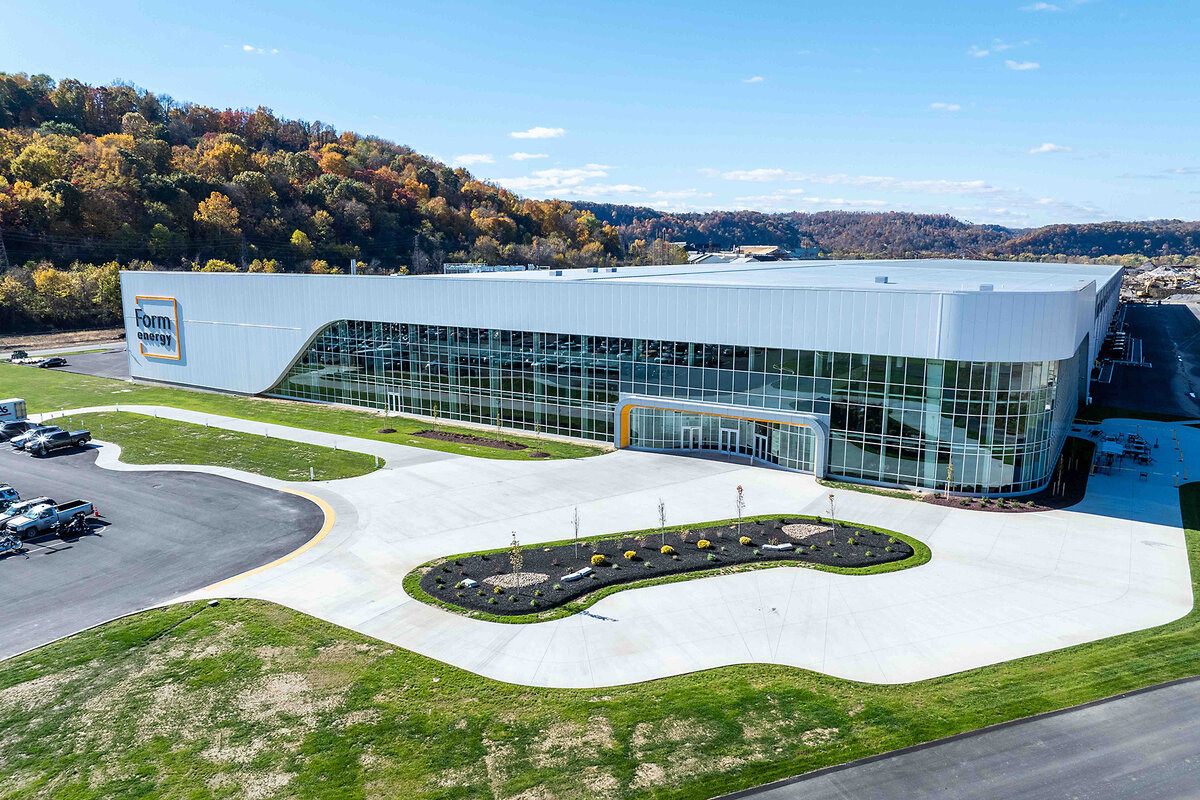 Large glass windows line the front side of Form Energy's facility, with a forested hill nearby.