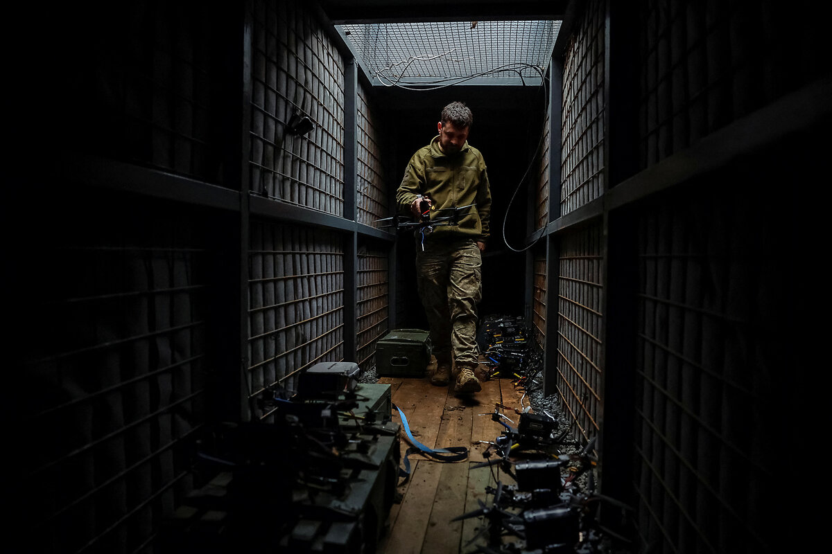 A member of the Ukrainian armed forces stands in an enclosed wire structure, preparing drones that will attack Russian defenses.
