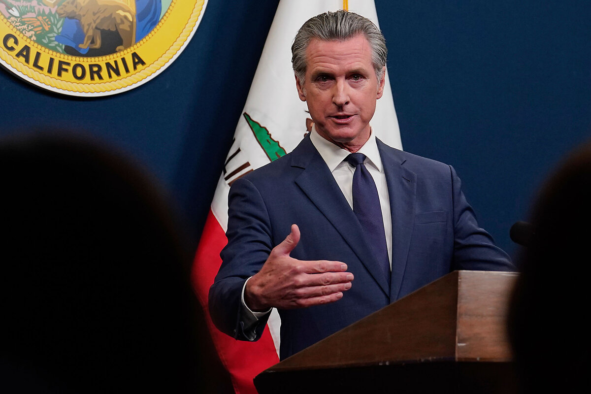 California Gov. Gavin Newsom, dressed in a dark blue suit, gestures as he speaks to reporters at a news conference.