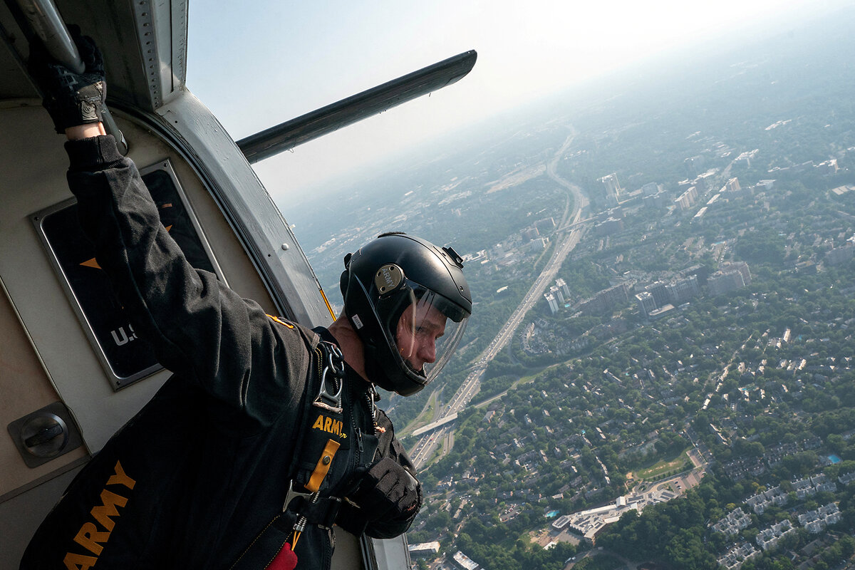 A member of the U.S. Army Golden Knights parachute team, leaning out of a helicopter, looks for his landing zone. 
