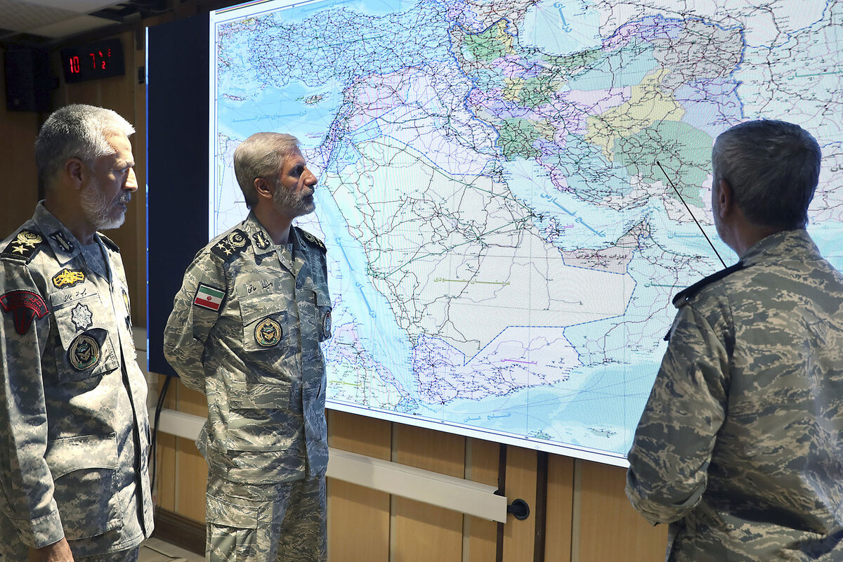 Three men in Iranian military uniforms stand looking at a large map of the Middle East.
