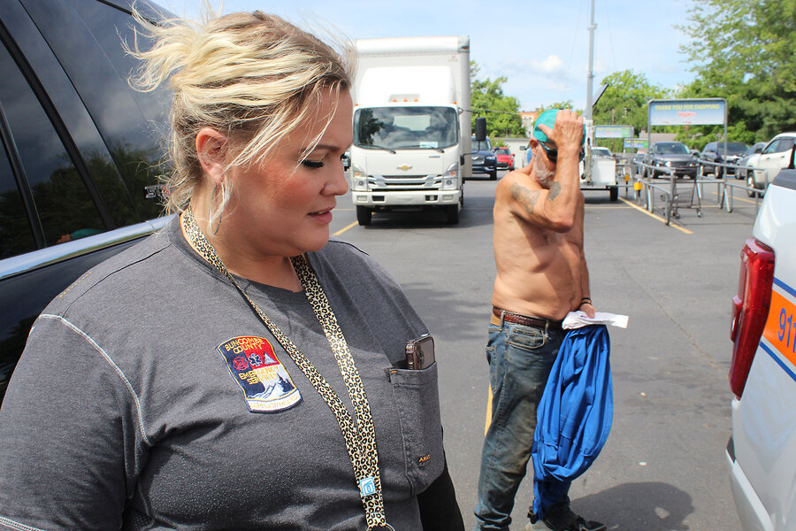 Brandi Hayes, who helps people fighting drug addiction, pictured in a parking lot, with a shirtless man standing nearby. 