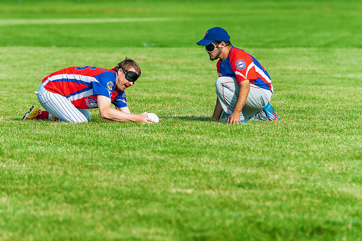 Teammates Richard Schultz and Daniel Hernandez kneel on the grass across from each other to field a ball.