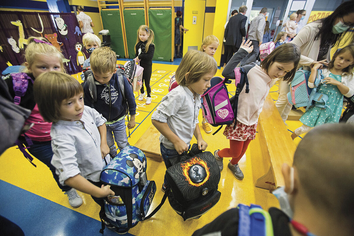Children carrying their backpacks enter a classroom with bright yellow floors on the first day of the school year in 2020.