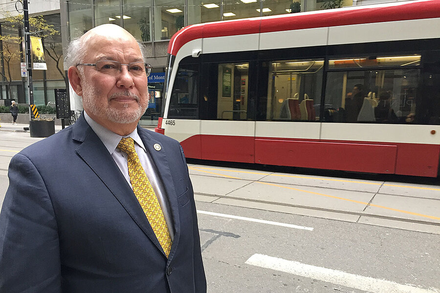Man in suit stands on city street with tram pictured in background.