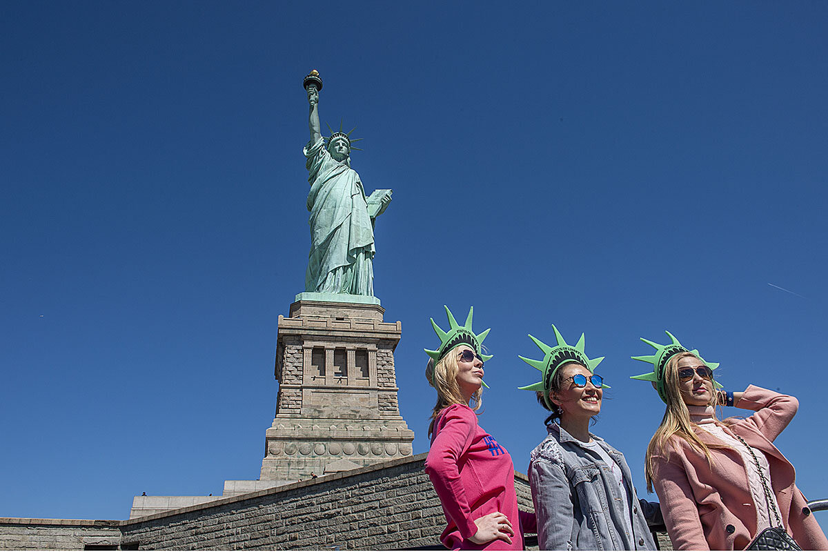 Visitors to Liberty Island pose for pictures in front of the Statue of Libe...