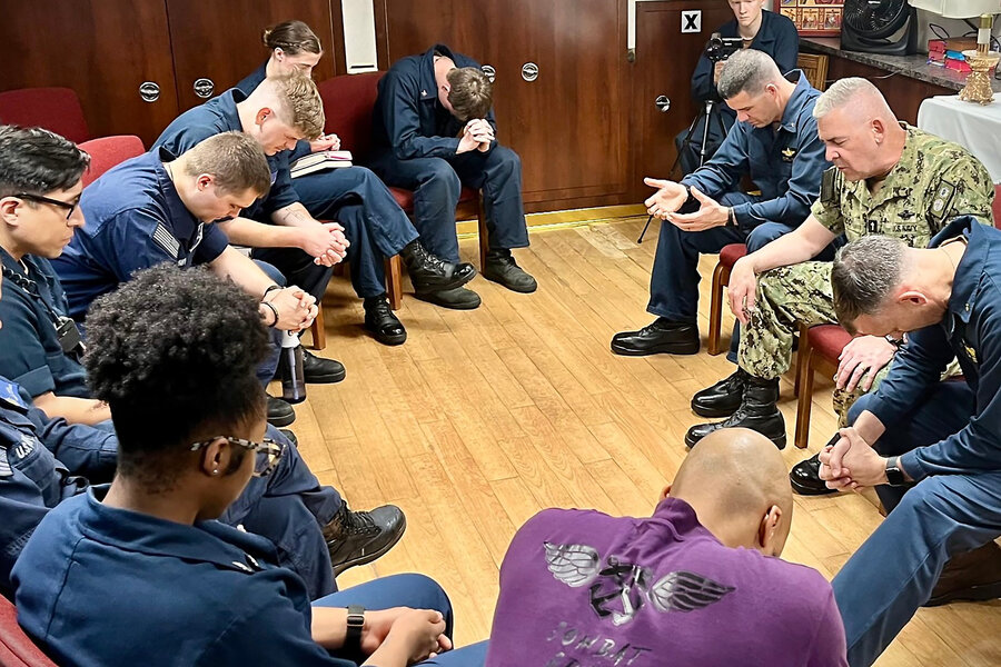 Blue-uniformed sailors sit in a circle to pray with Rear Adm. Gregory Todd.