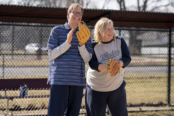 Actors Jeff Hiller and Bridget Everett stand together smiling and wearing baseball gloves in a scene from the TV series “Somebody Somewhere.”