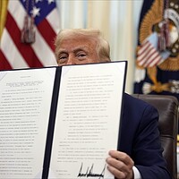 President Donald Trump holds an executive order in the Oval Office of the White House. The document blocks the lower half of his face.