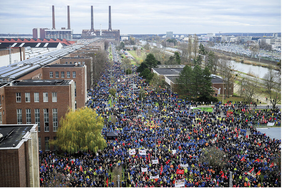 Protesters amass outside the Volkswagen plant in Wolfsburg, Germany. Some hold signs and banners.