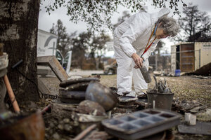 Pauline Solliday, wearing white protective clothing, bends over to inspect debris salvaged from her Altadena, California, home, which was destroyed by the Eaton Fire in January 2025. 