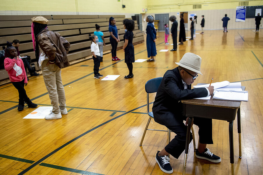 Sixth grader Da'Merion Whitiker sits at a desk full of notebooks in a school gym, waiting to speak about poet Langston Hughes.