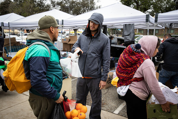 Nathaniel Whitfield, in a gray jacket with a hood, helps people pick up food and other items at the Pasadena Community Job Center Feb. 12, 2025, in Pasadena, California. He teaches in the department of world arts, cultures, and dance at UCLA. 