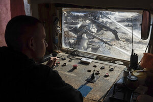 A worker sits at controls, with a view of mining operations.