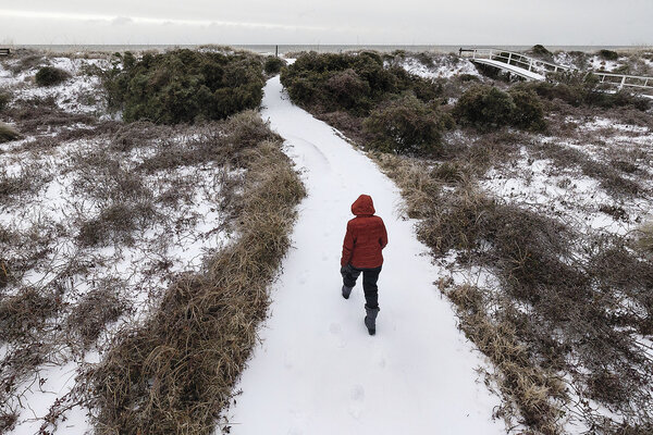 A person in a hooded coat walks down a snowy path toward the ocean on the Isle of Palms, South Carolina, Jan. 22, 2025.