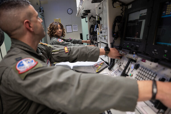 Two missileers make eye contact as they synchronize the turning of keys on a control panel.