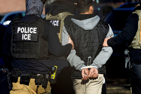 A handcuffed man is led away by U.S. Immigration and Customs Enforcement.