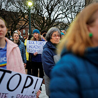 Protesters supporting Dr. Rasha Alawieh stand outdoors, some carrying signs.