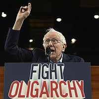 Bernie Sanders raises his arm as he speaks, with a 'fight oligarchy' sign on the podium.