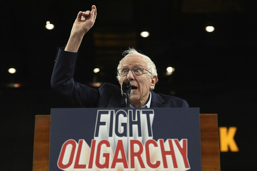 Bernie Sanders raises his arm as he speaks, with a 'fight oligarchy' sign on the podium.