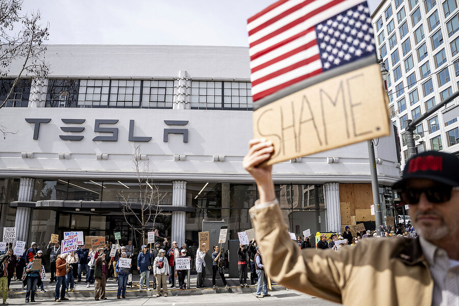 With other protesters in the background, a man holds up a sign with an upside-down U.S. flag and the word 'shame.'