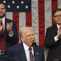 Donald Trump speaks as Vice President JD Vance and House Speaker Mike Johnson stand behind him, clapping.