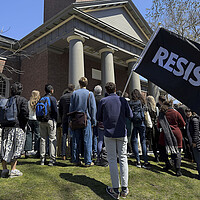 Harvard University community members, one with a 'resist' flag, gather at a rally on campus 