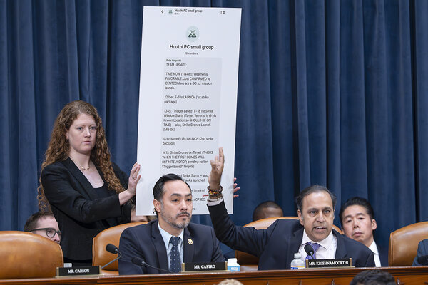 From his seat in front of a blue curtain, Illinois Rep. Raja Krishnamoorthi points to a chart displaying a text message by Defense Secretary Pete Hegseth
