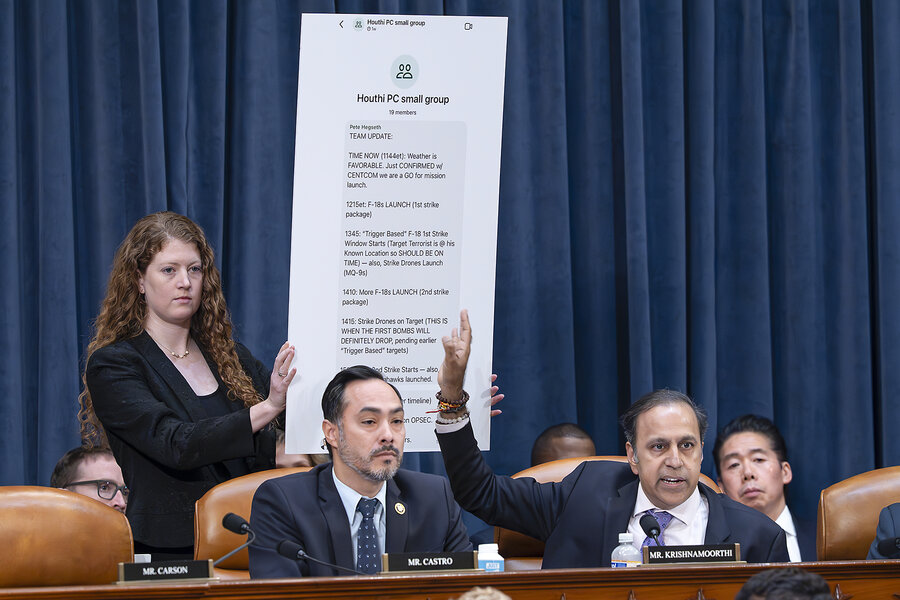 From his seat in front of a blue curtain, Illinois Rep. Raja Krishnamoorthi points to a chart displaying a text message by Defense Secretary Pete Hegseth