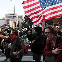 Demonstrators holding an American flag rush forward after being shot at during protests against federal immigration sweeps.